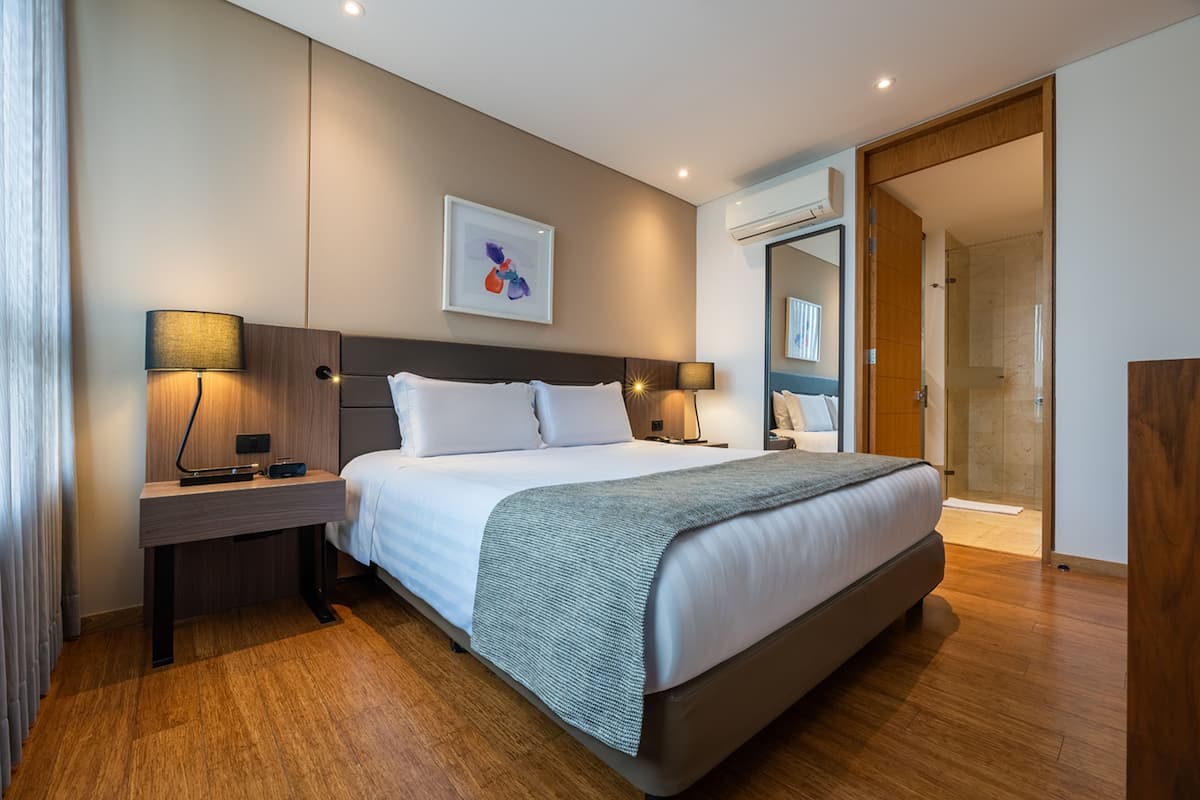 A modern hotel room with a large bed, bedside tables, a wall-mounted artwork, and a glass shower area.