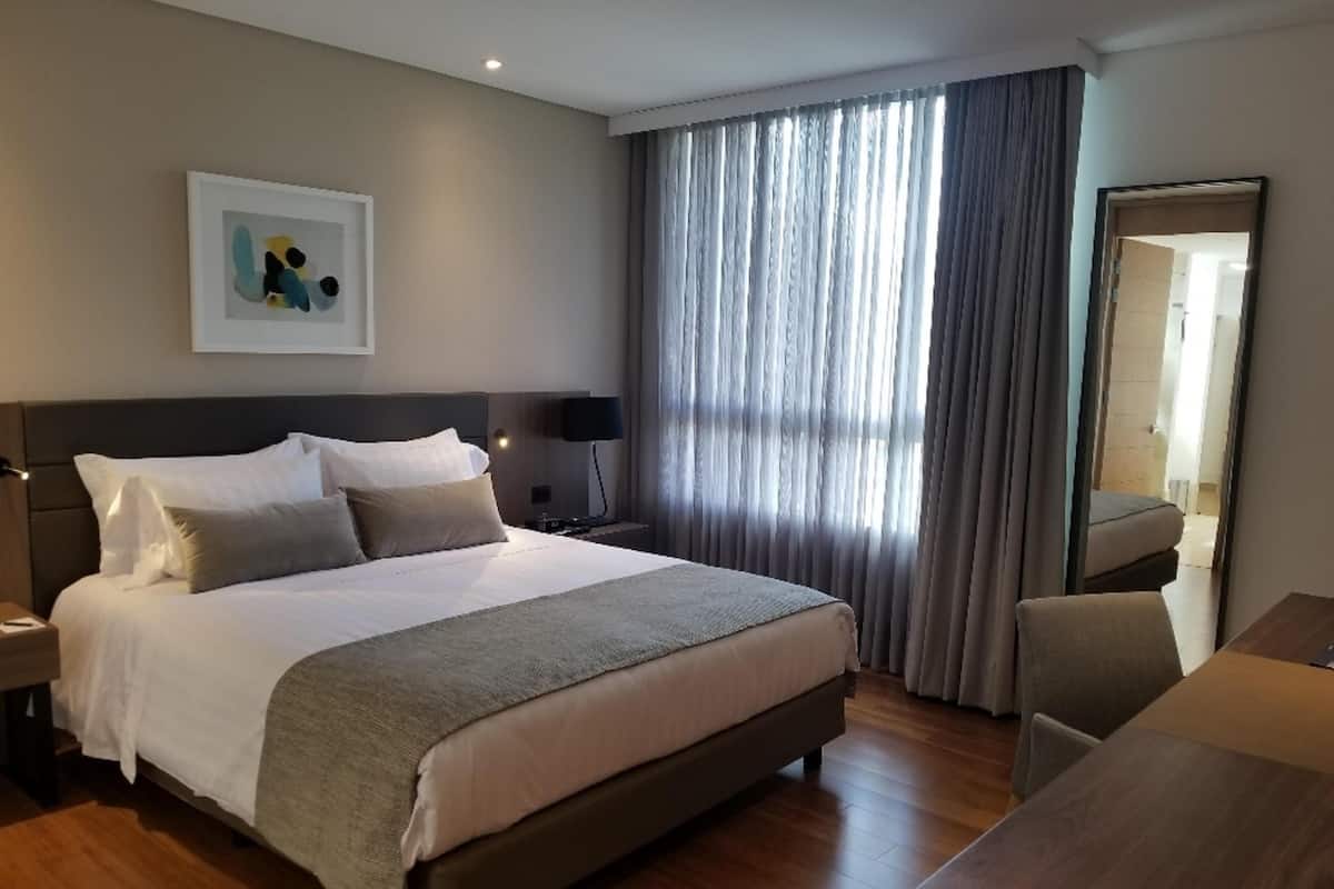 A modern hotel room with a large bed, a desk, and a mirror.