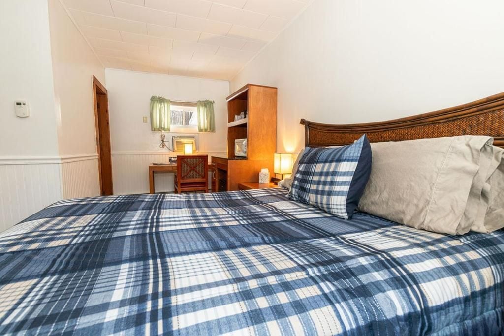 A bedroom with a bed, bedside table, lamp, and a small desk with a chair.