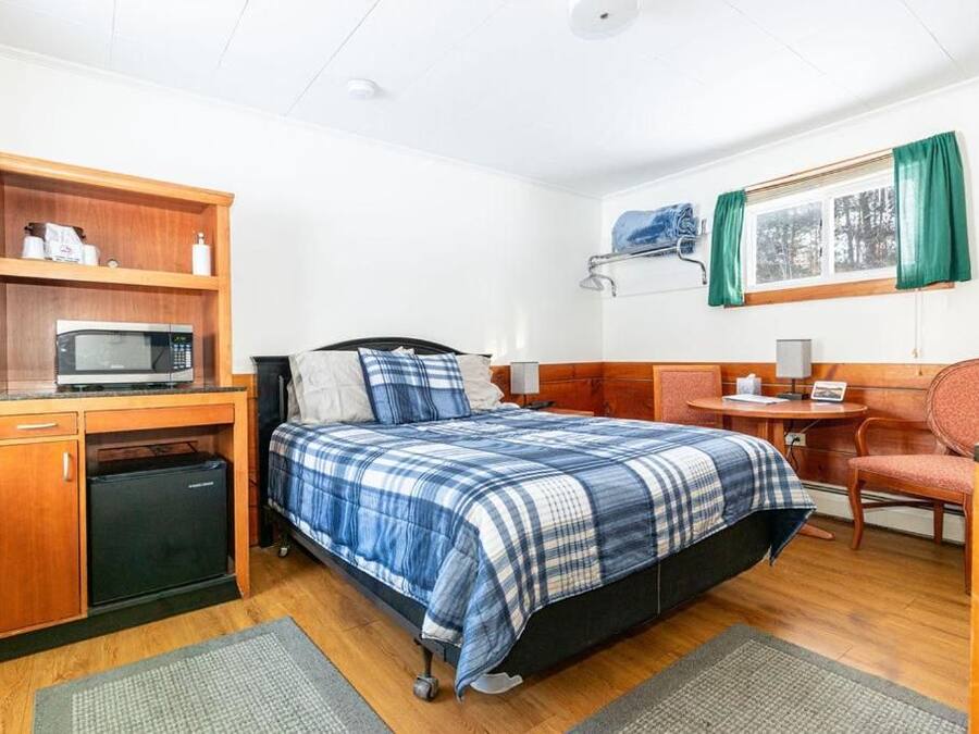 A compact room with a bed, a desk, a small refrigerator, and a shelf with toiletries.