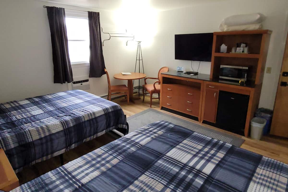 A room with two beds, a desk, a chair, a television, and a microwave.