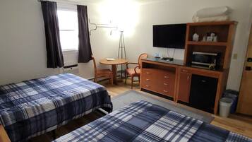 A room with two beds, a desk, a chair, a television, and a microwave.