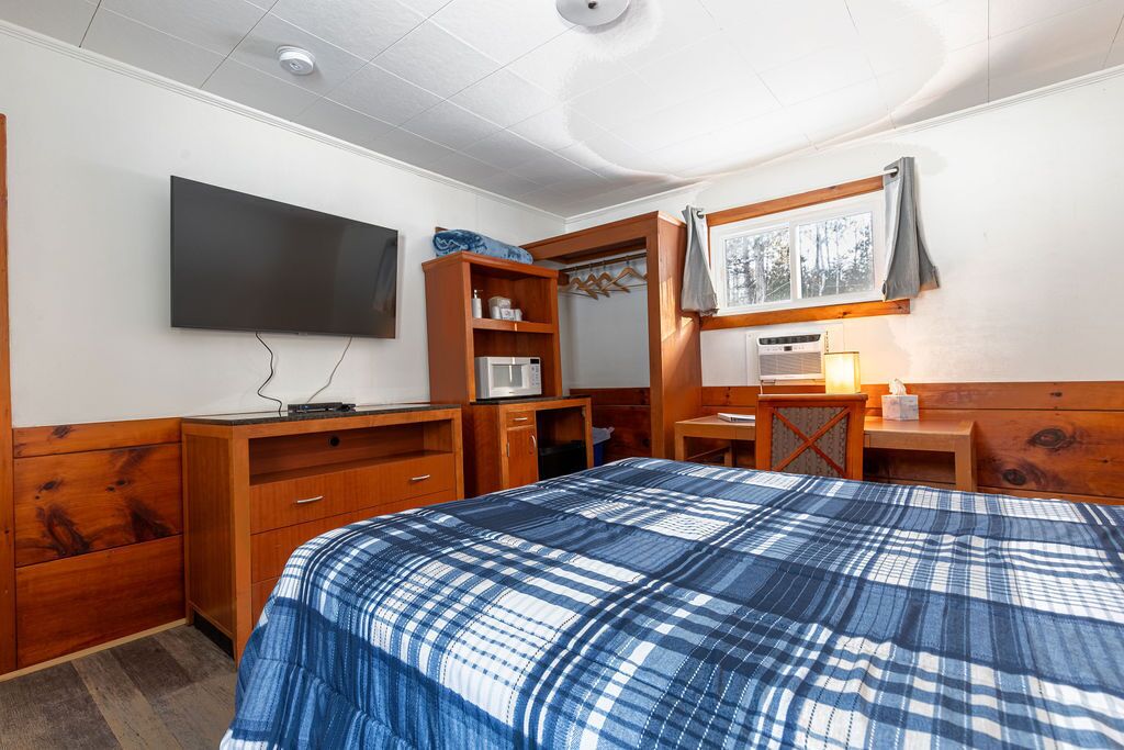 Un dormitorio con cama, televisión, armario, escritorio y ventana.