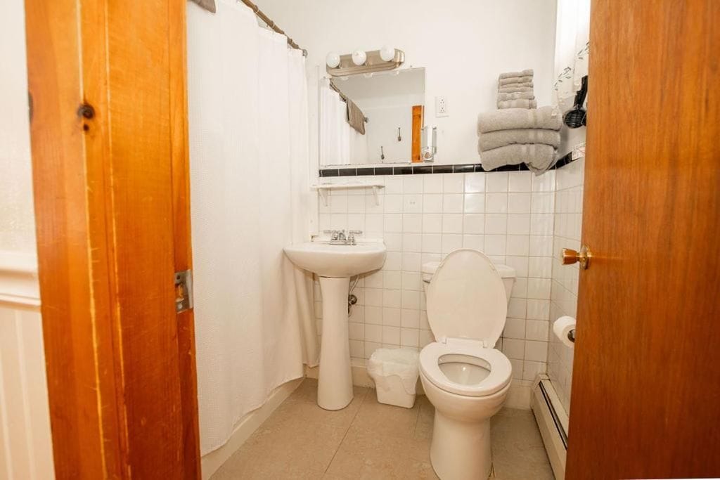 Un baño con lavamanos blanco, inodoro y espejo sobre el lavamanos.