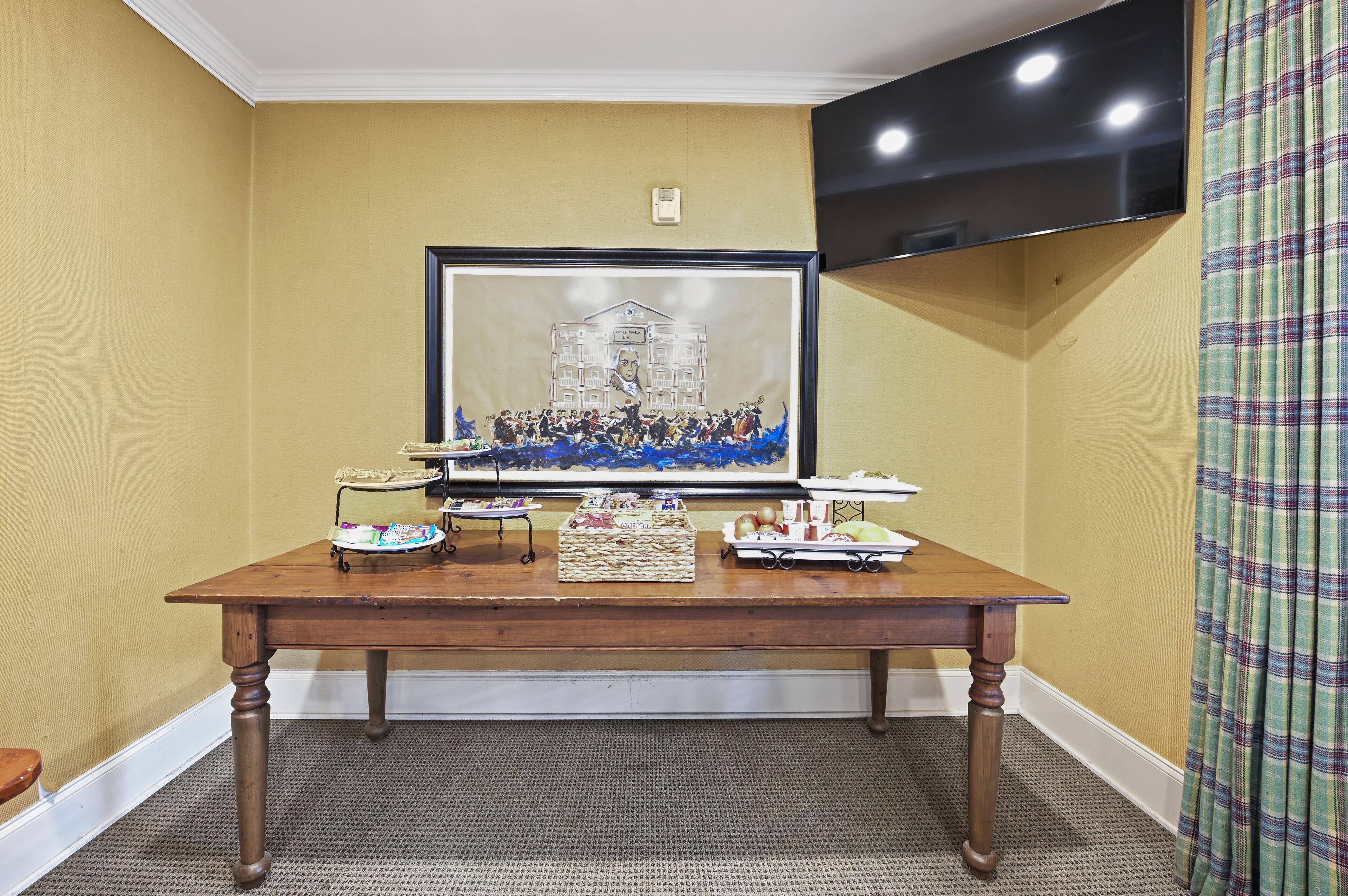 A room with a wooden table, a framed artwork, and a flat-screen TV mounted on the wall.