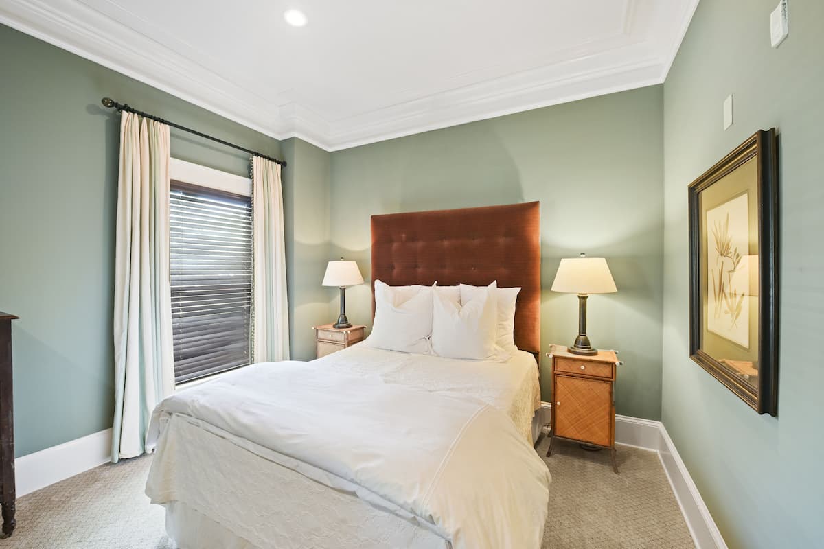 A neatly made bed with white linens, a wooden headboard, and two bedside lamps.