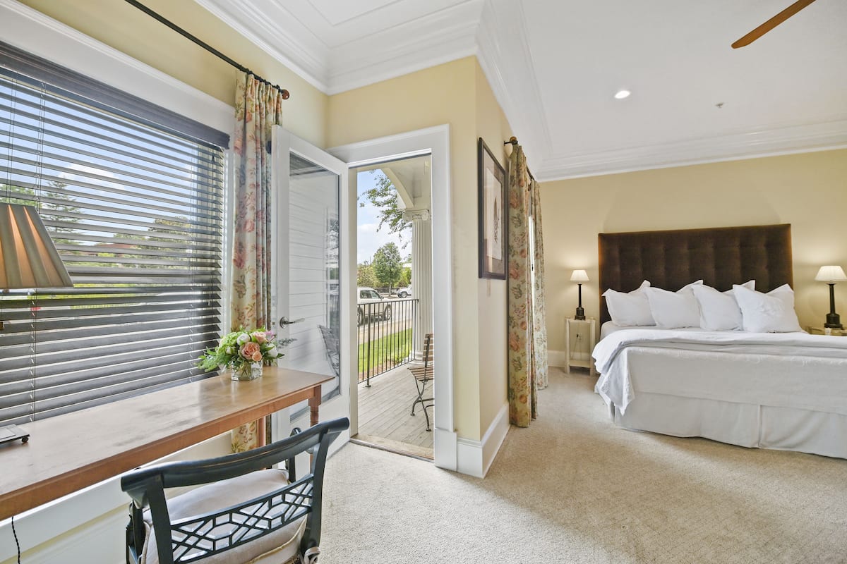 A bedroom with a large bed, a desk with a chair, and a view of the outside through a door.