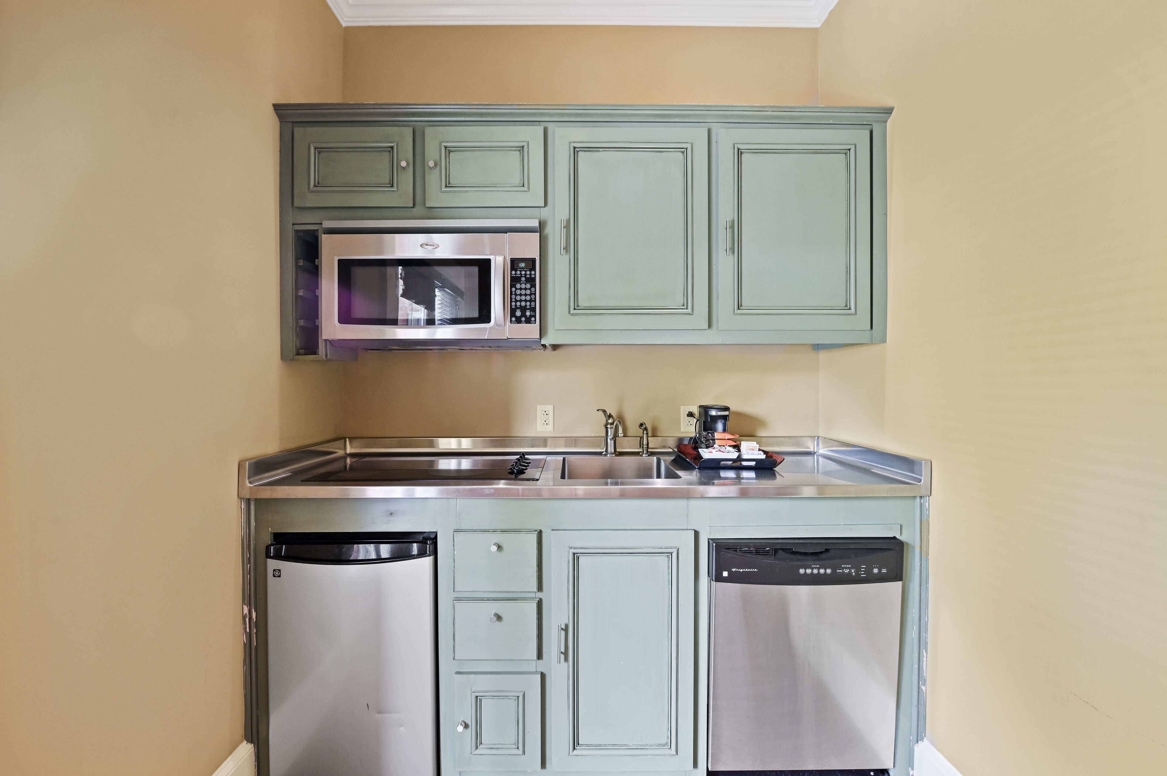 A compact kitchen with green cabinets, a stainless steel microwave, and a dishwasher.