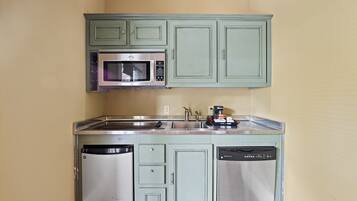 A compact kitchen with green cabinets, a stainless steel microwave, and a dishwasher.