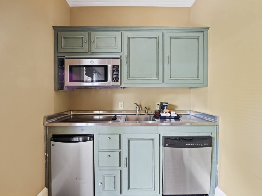 A compact kitchen with green cabinets, a stainless steel microwave, and a dishwasher.