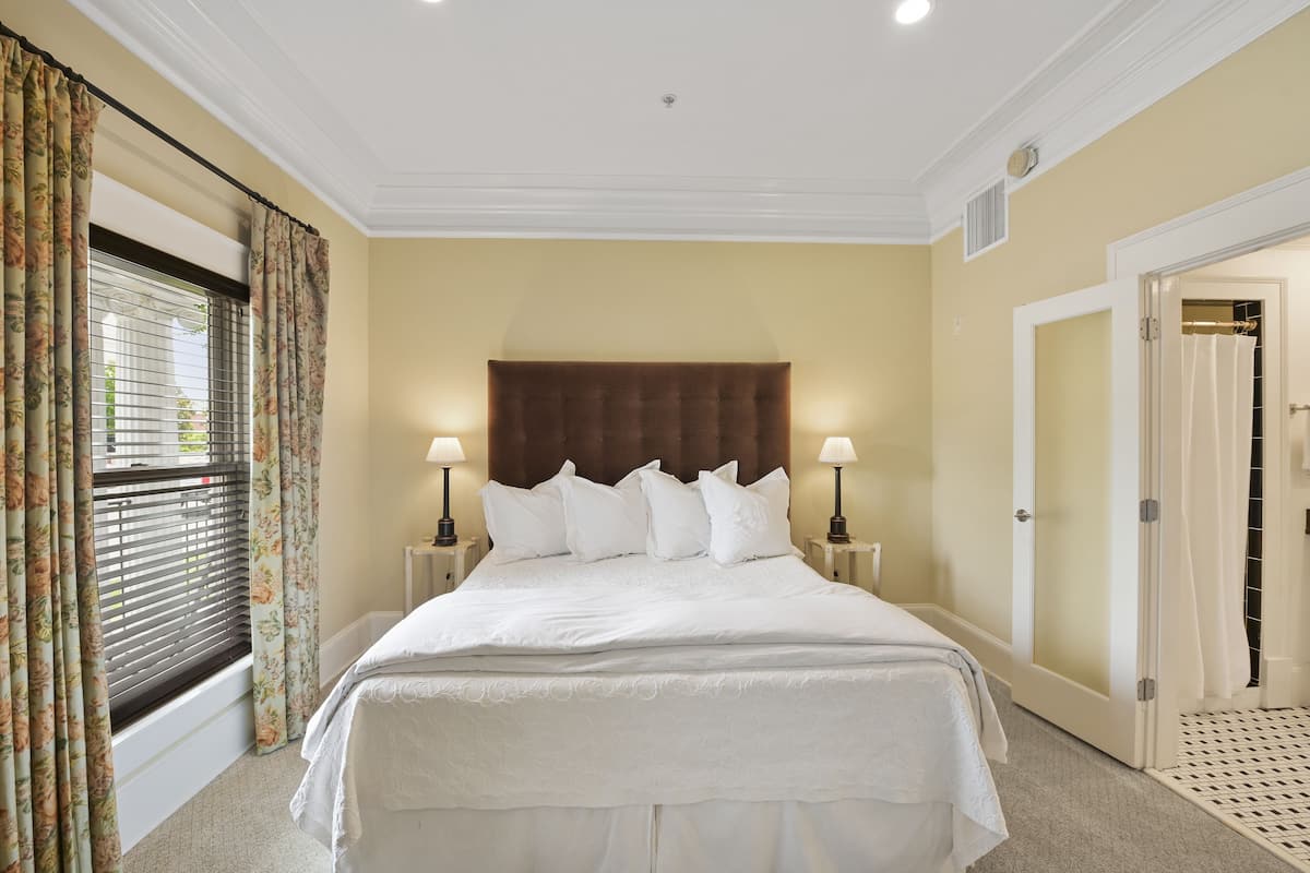 A neatly made bed with white linens, a brown headboard, and two bedside lamps.