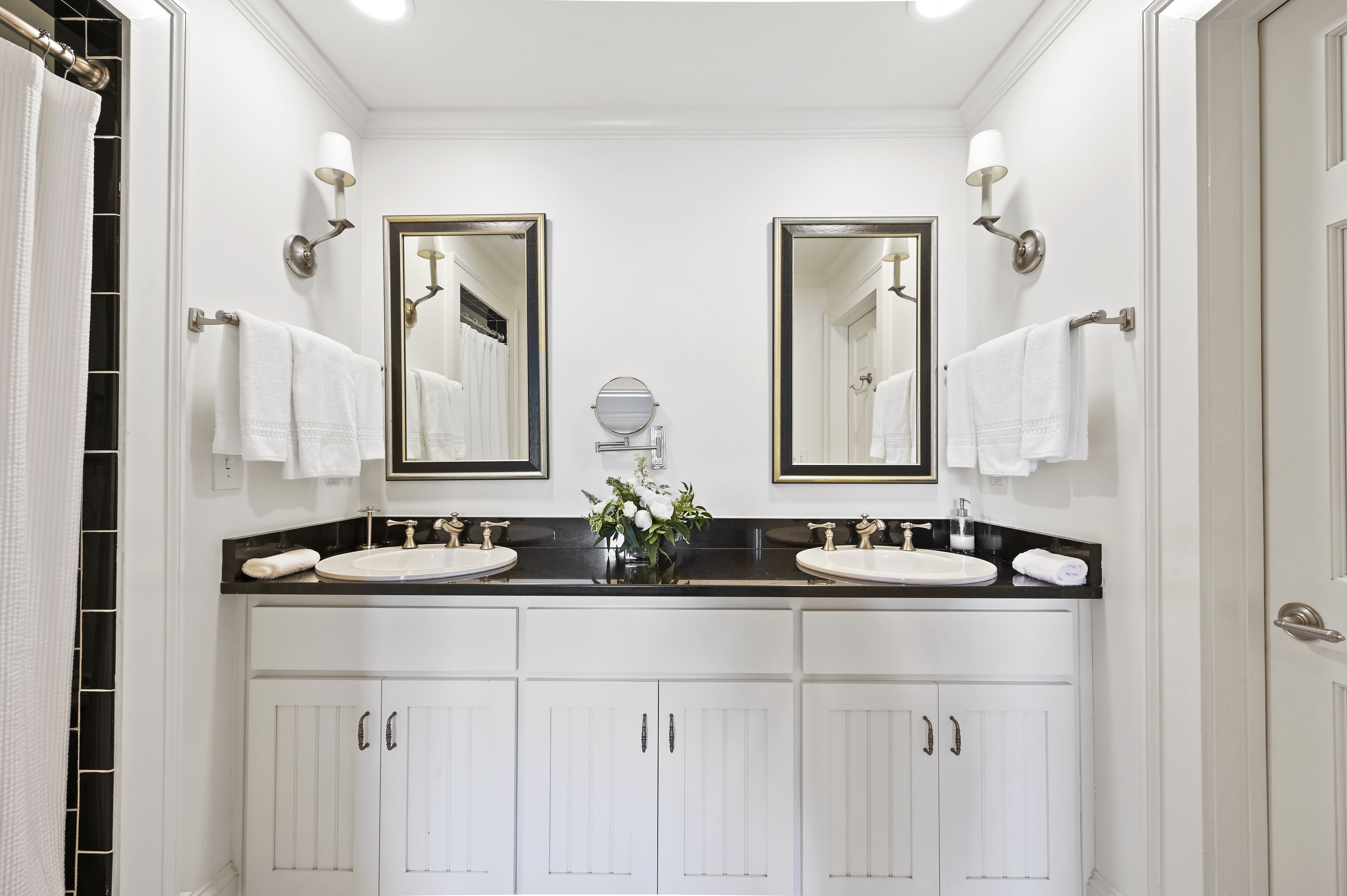A bathroom with two sinks, a mirror, and a vase with flowers.