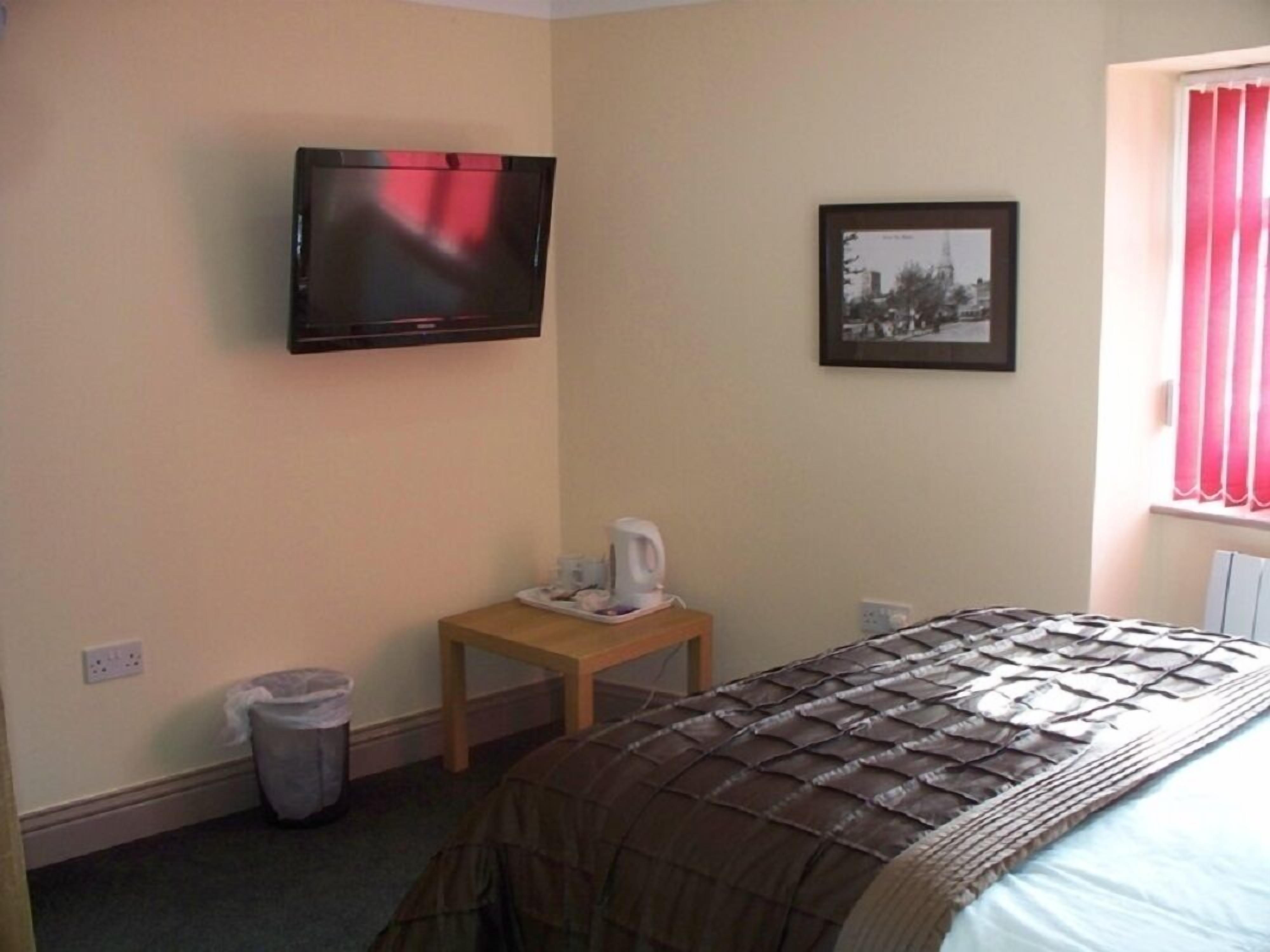 A hotel room with a bed, a TV mounted on the wall, a small table with a coffee maker, a picture frame on the wall, and a window with curtains.