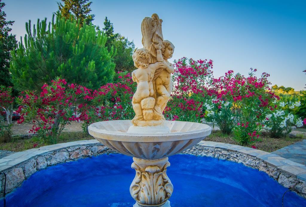 Ein Steinsbrunnen mit einer Statue einer Frau, die ein Kind hält, umgeben von einem Becken und bunten Blumen.