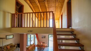 A spacious living area with a high ceiling, wooden staircase, and a dining area with a table and chairs. - Villa Elatia (Zakynthos)