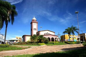 A church with a tall bell tower, surrounded by palm trees and a paved walkway. - Hotel Saron (Luziania)