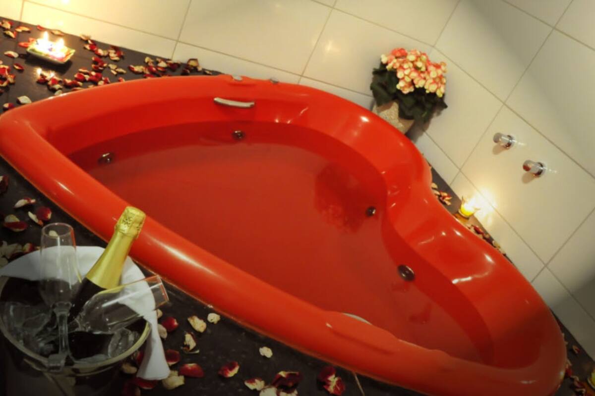 Un jacuzzi rojo con pétalos de rosa y champán.