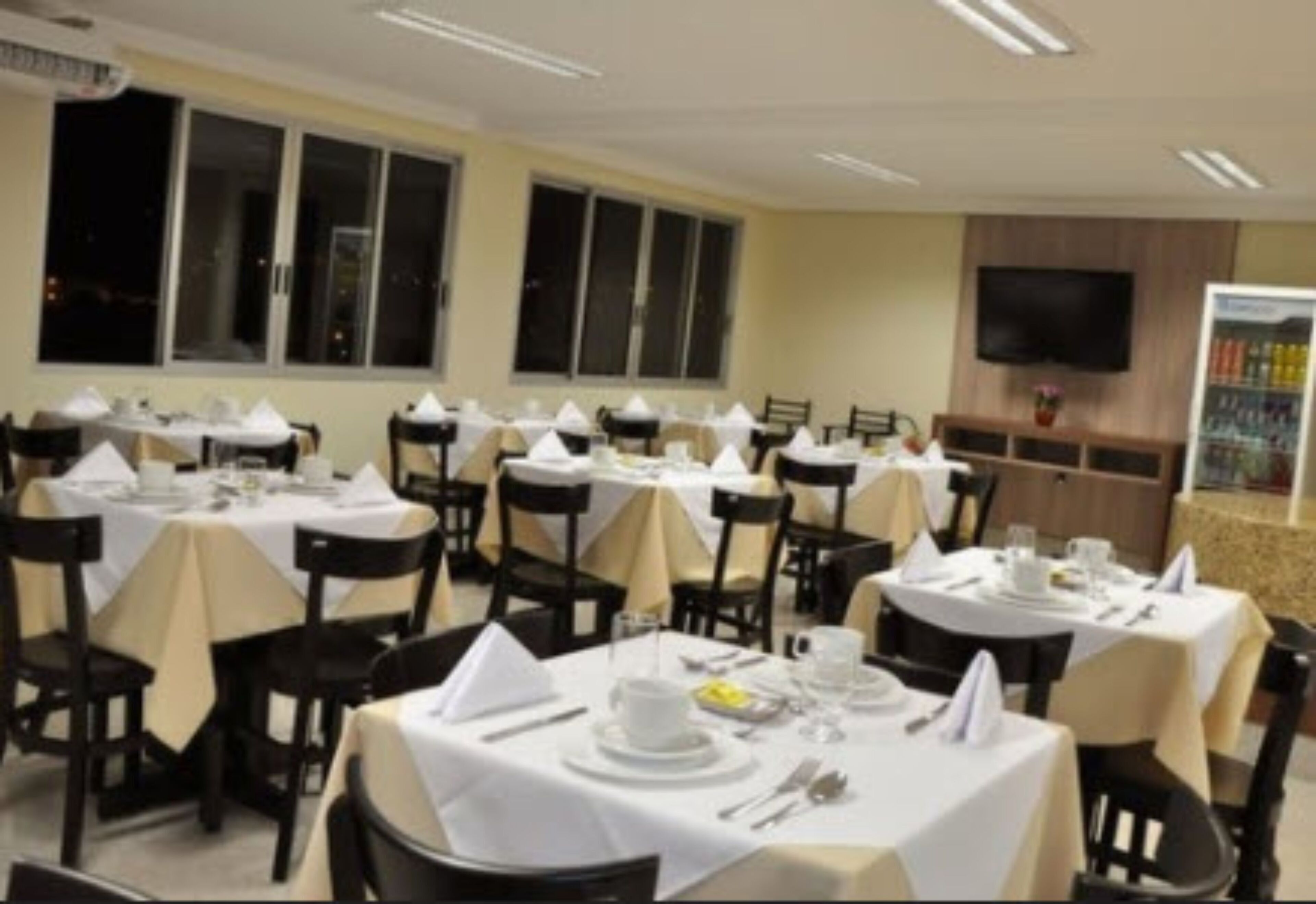 A restaurant with round tables covered in white tablecloths, black chairs, and neatly set dining tables with plates, glasses, and cutlery.