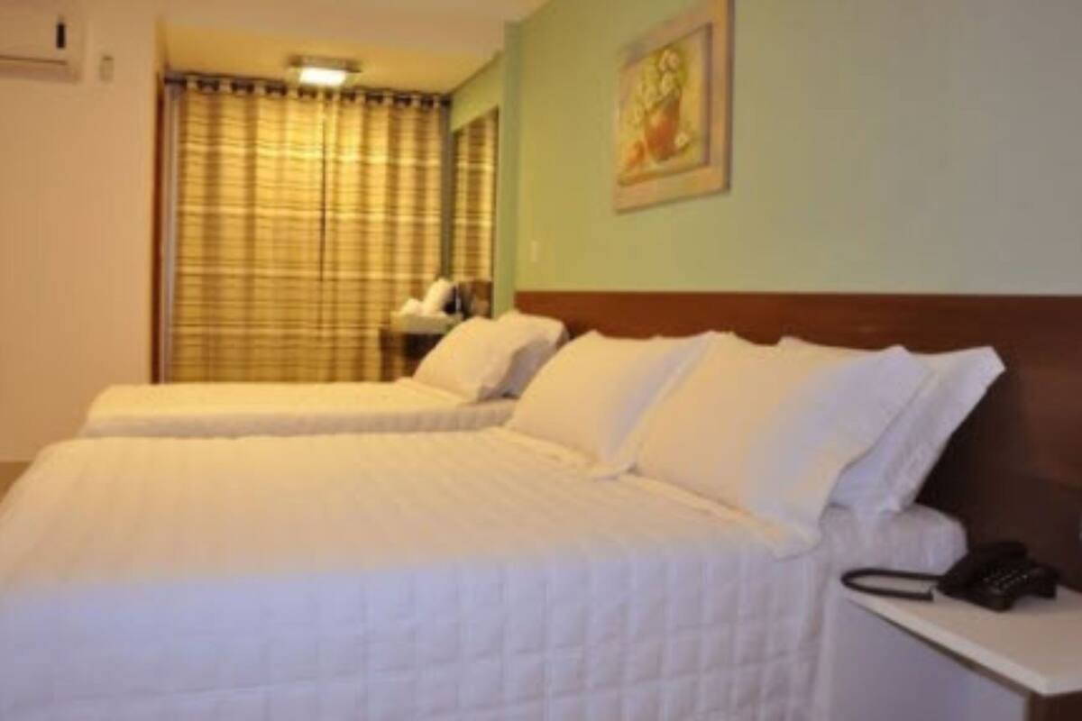 Una habitación de hotel con dos camas, una mesita de noche con teléfono y una ventana con cortinas.