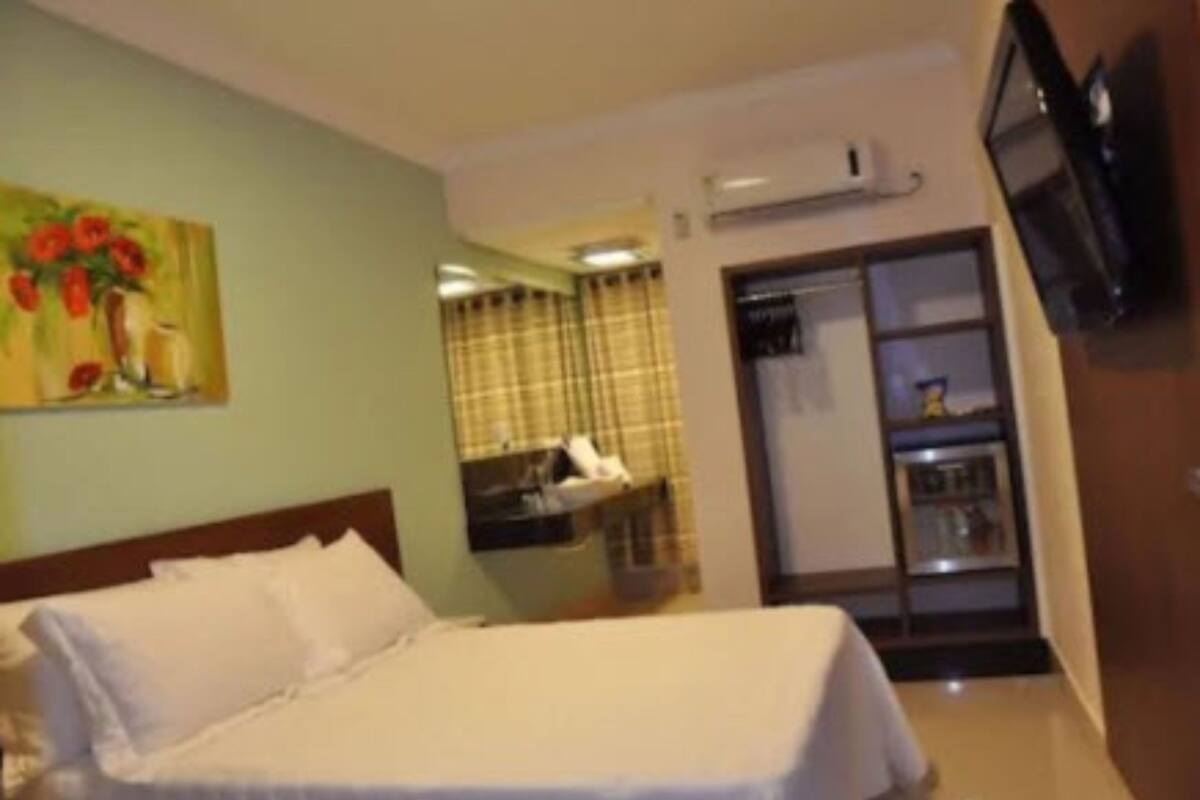 Habitación de hotel con cama, un cuadro de flores, televisión y baño con espejo y cortinas.