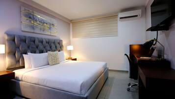 A modern bedroom with a tufted headboard, a large bed, bedside lamps, a desk with a chair, and a mounted air conditioner.