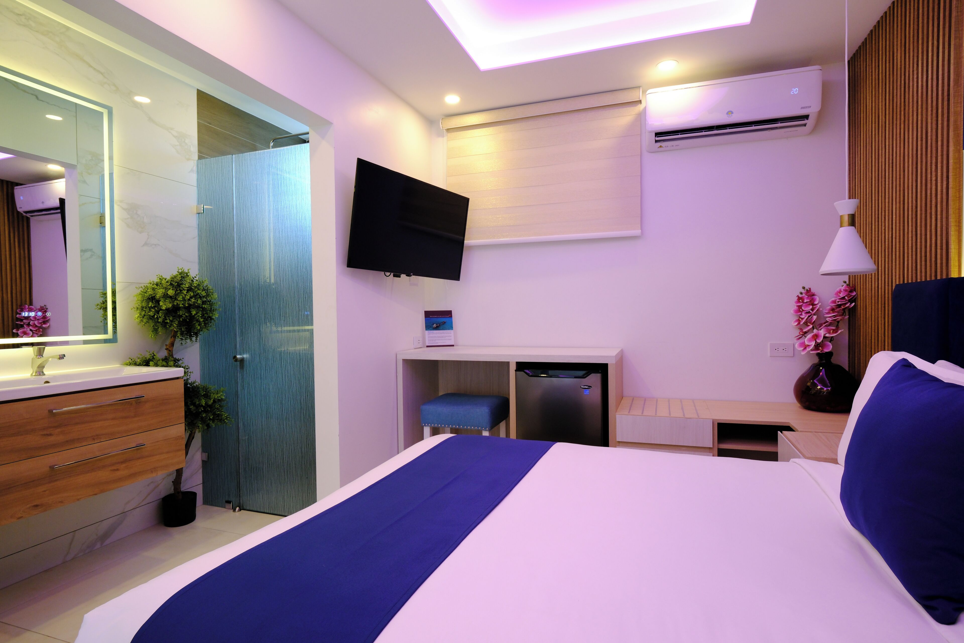 Een moderne hotelkamer met een groot bed, een bureau met een computer, een flatscreen-tv, een klein zithoekje en een badkamer met een spiegel en wastafel.