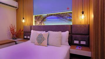 Ein Hotelzimmer mit einem großen Bett, einem Nachttisch mit Lampe, einer Wand-Klimaanlage und einem Wandgemälde, das eine Brücke und Bäume zeigt.