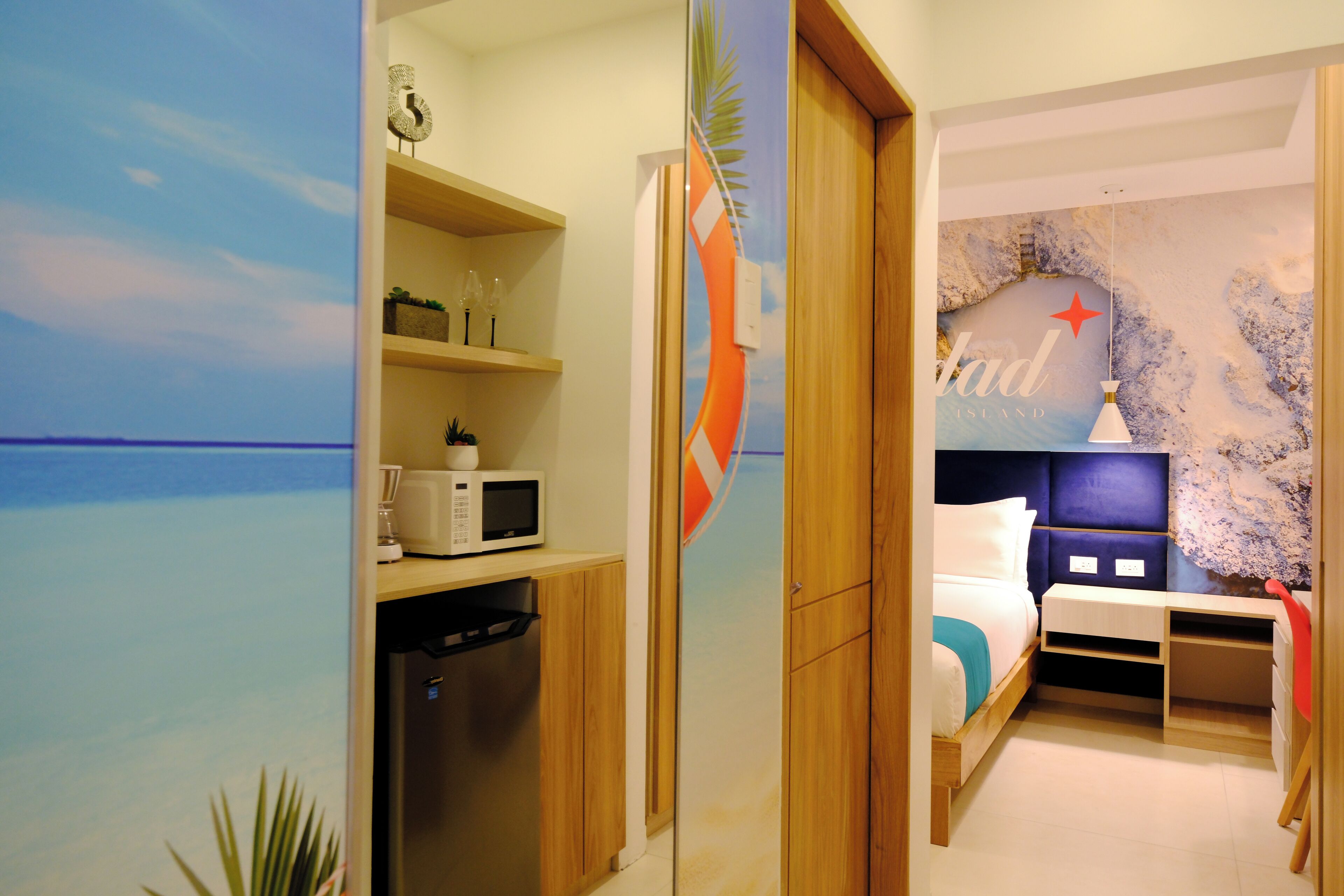 A bedroom with a bed, a nightstand, a dresser, a microwave, and a shelf with decorative items.