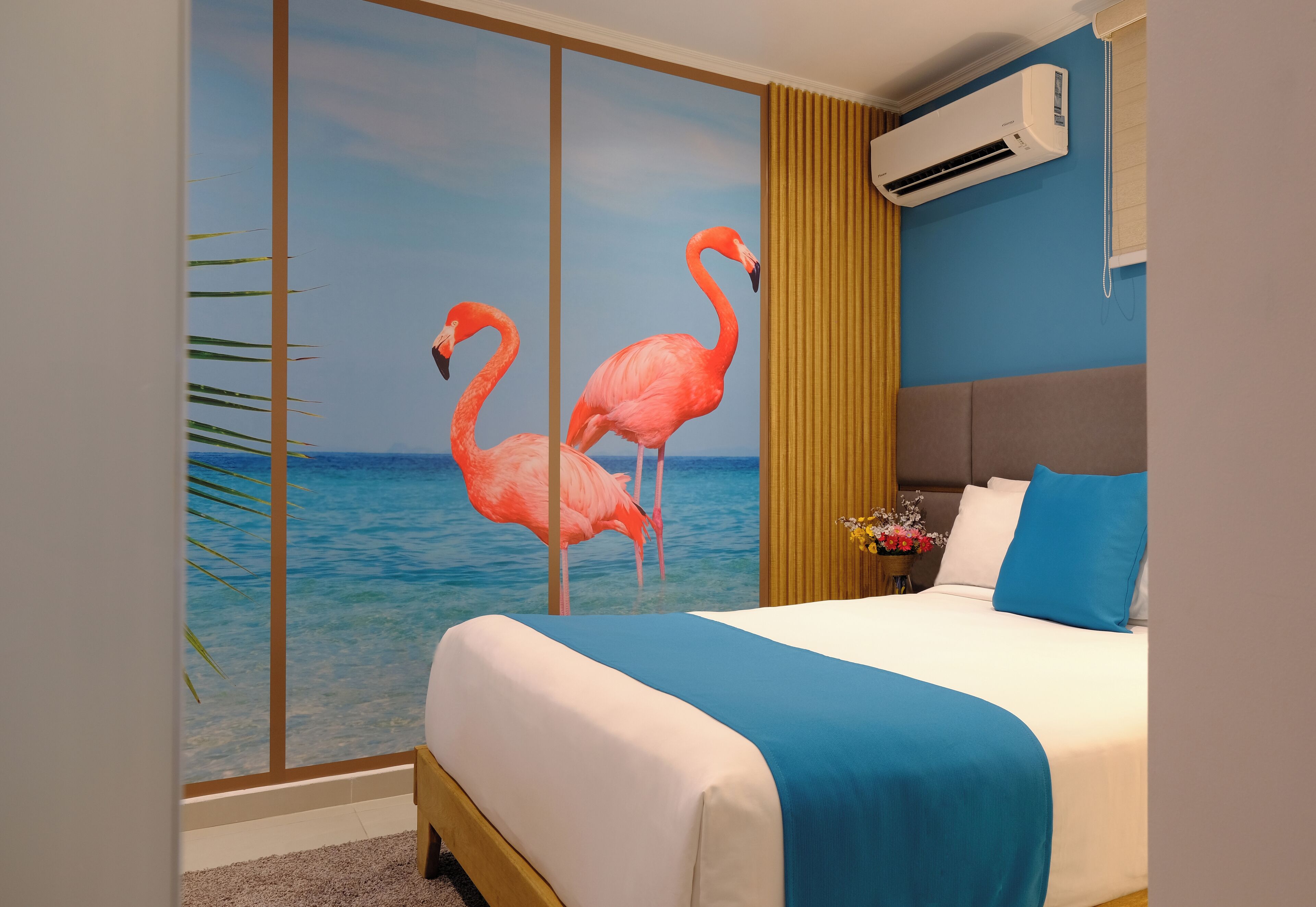 Quarto de hotel com cama, uma janela grande com vista para o mar e um mural de flamingos na parede.