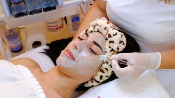 A person receiving a facial treatment in a medical setting with a white towel and a branded towel on the bed.