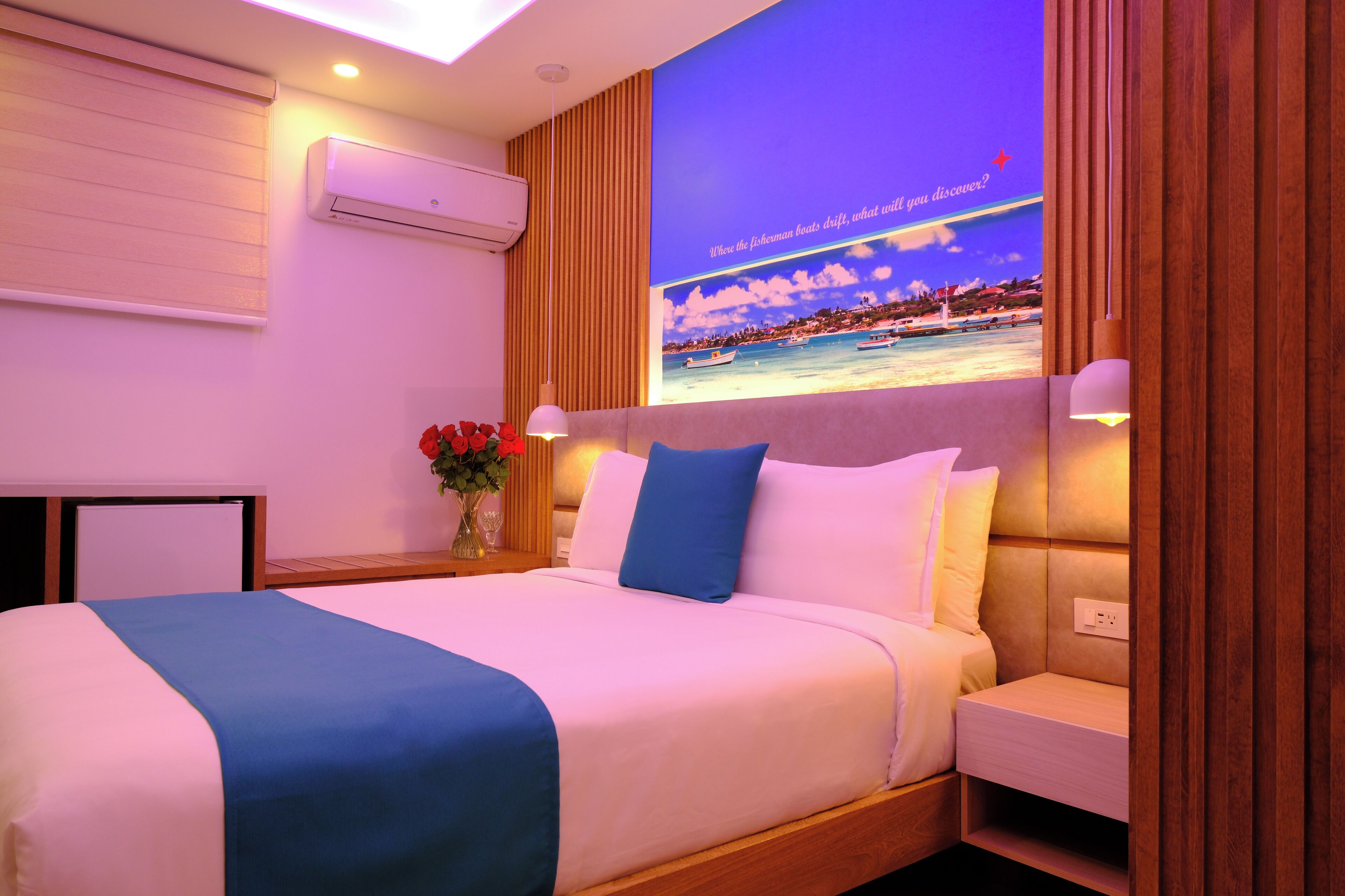 A hotel room with a bed, bedside table, lamp, and a wall-mounted TV displaying a scenic view.