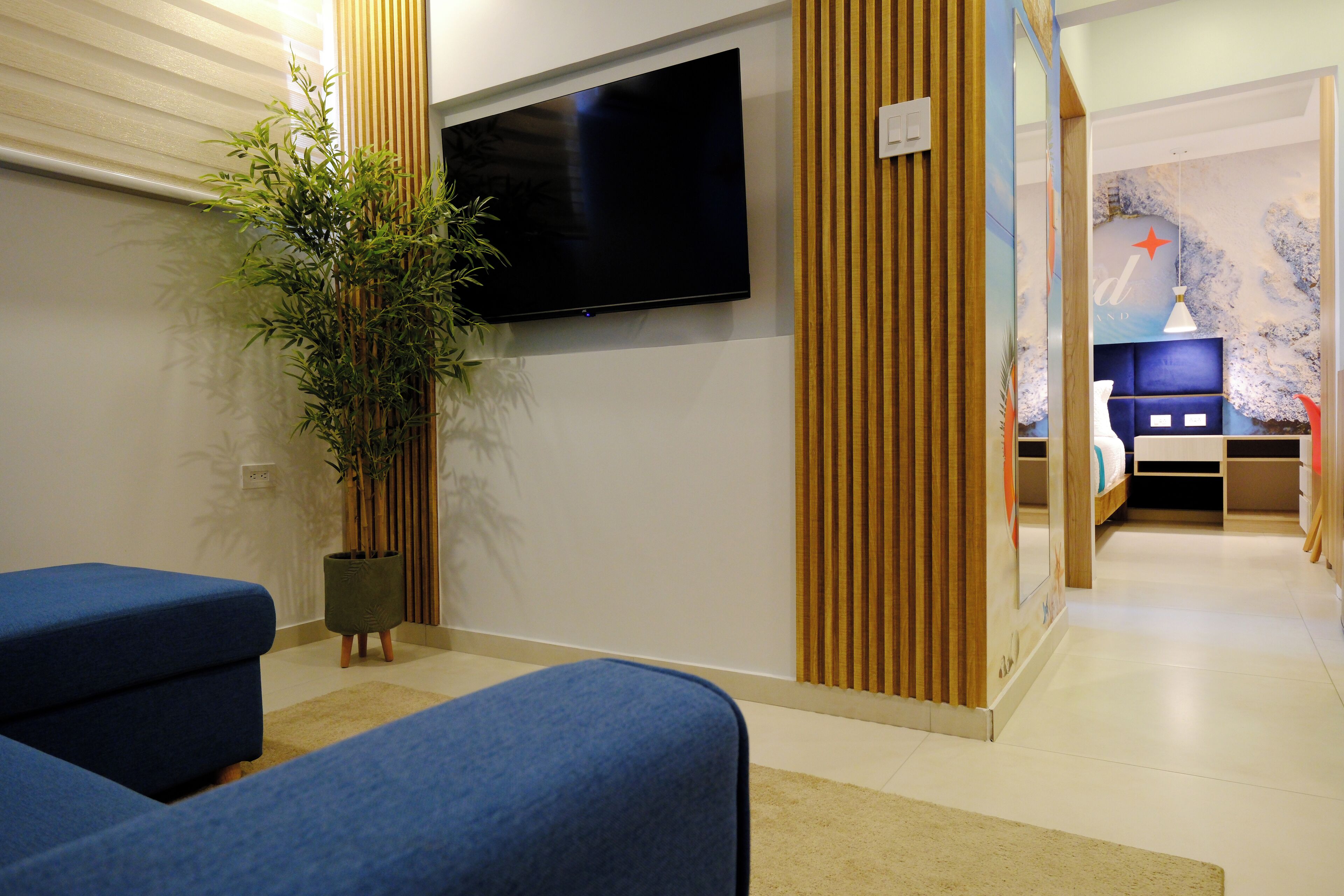Una sala de estar moderna con un televisor de pantalla plana, una planta grande en maceta y un sofá azul.