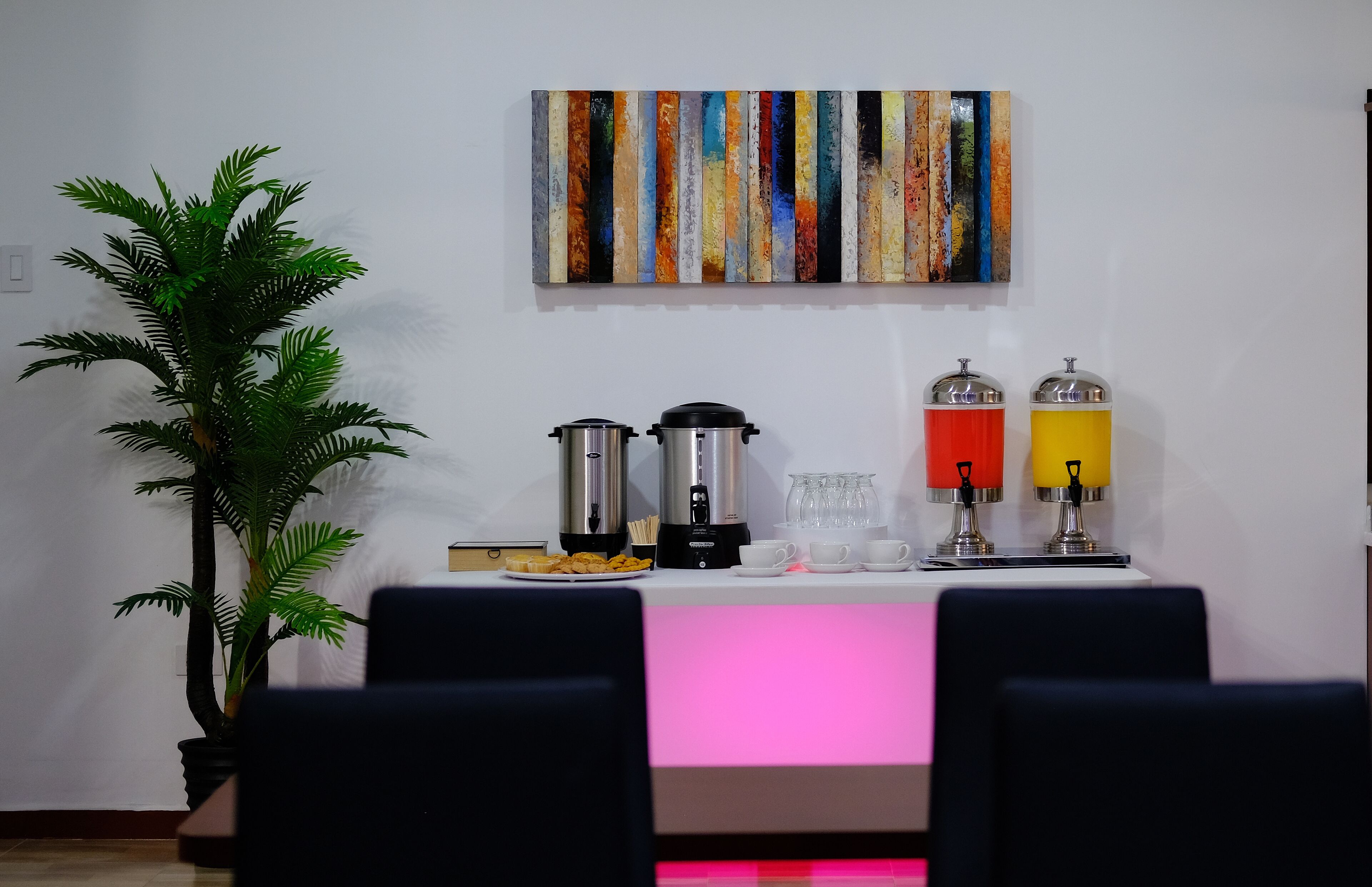 Un coin repas avec une table dressée pour deux personnes, une machine à café, un distributeur d’eau et une plante en pot.