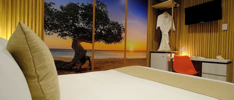 A hotel room with a bed, a desk, a TV, and a view of a sunset over the ocean.