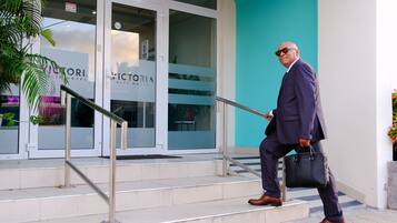 A man in a suit walking up the stairs to a hotel entrance with a sign reading "Victoria City Hotel".