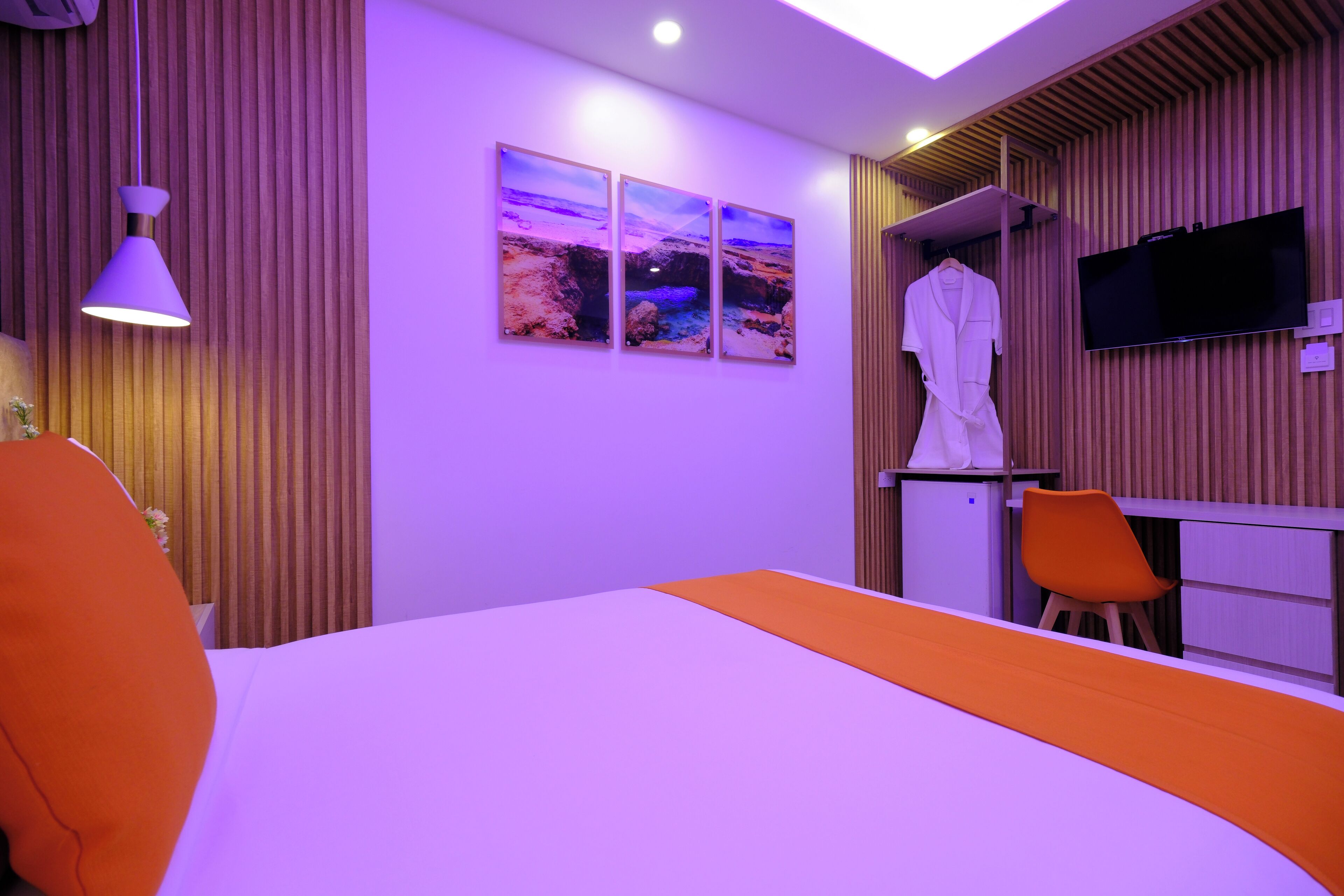 A modern hotel room with a large bed, a flat-screen TV, a robe, and a small seating area.