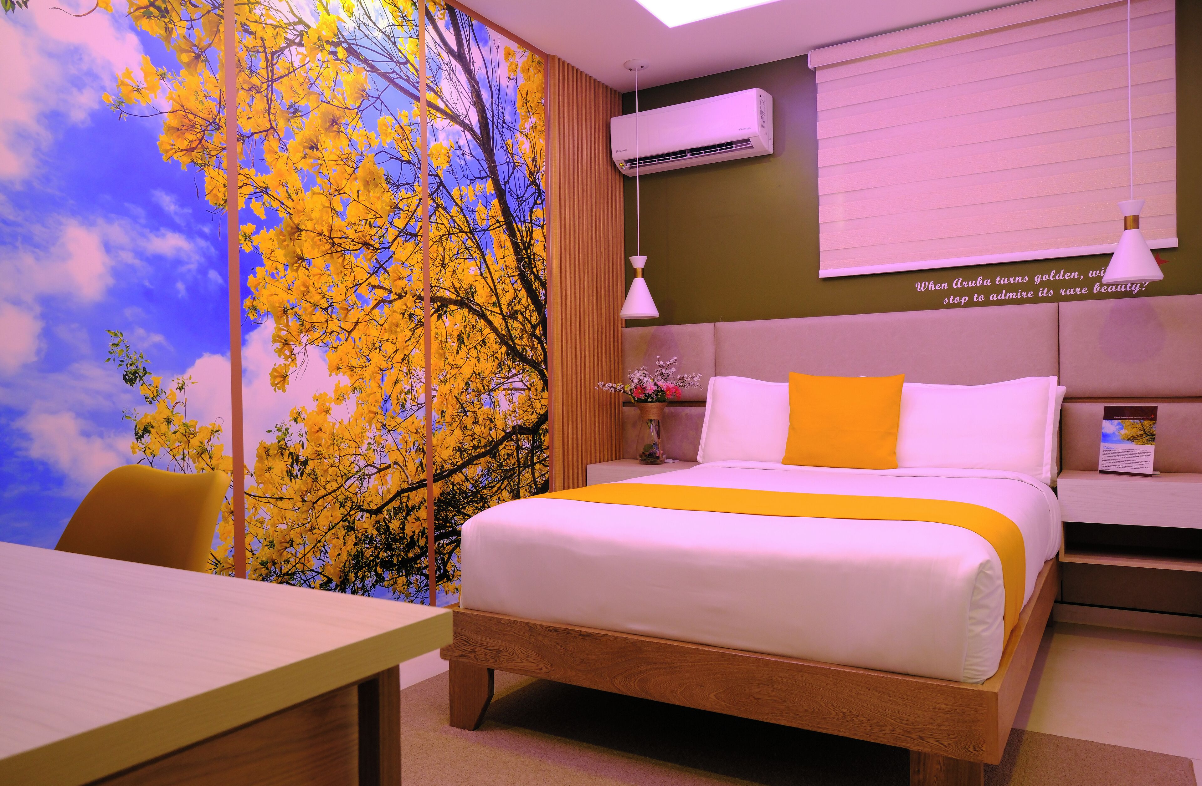 A hotel room with a bed, a desk, a chair, a nightstand, and a wall with a mural.