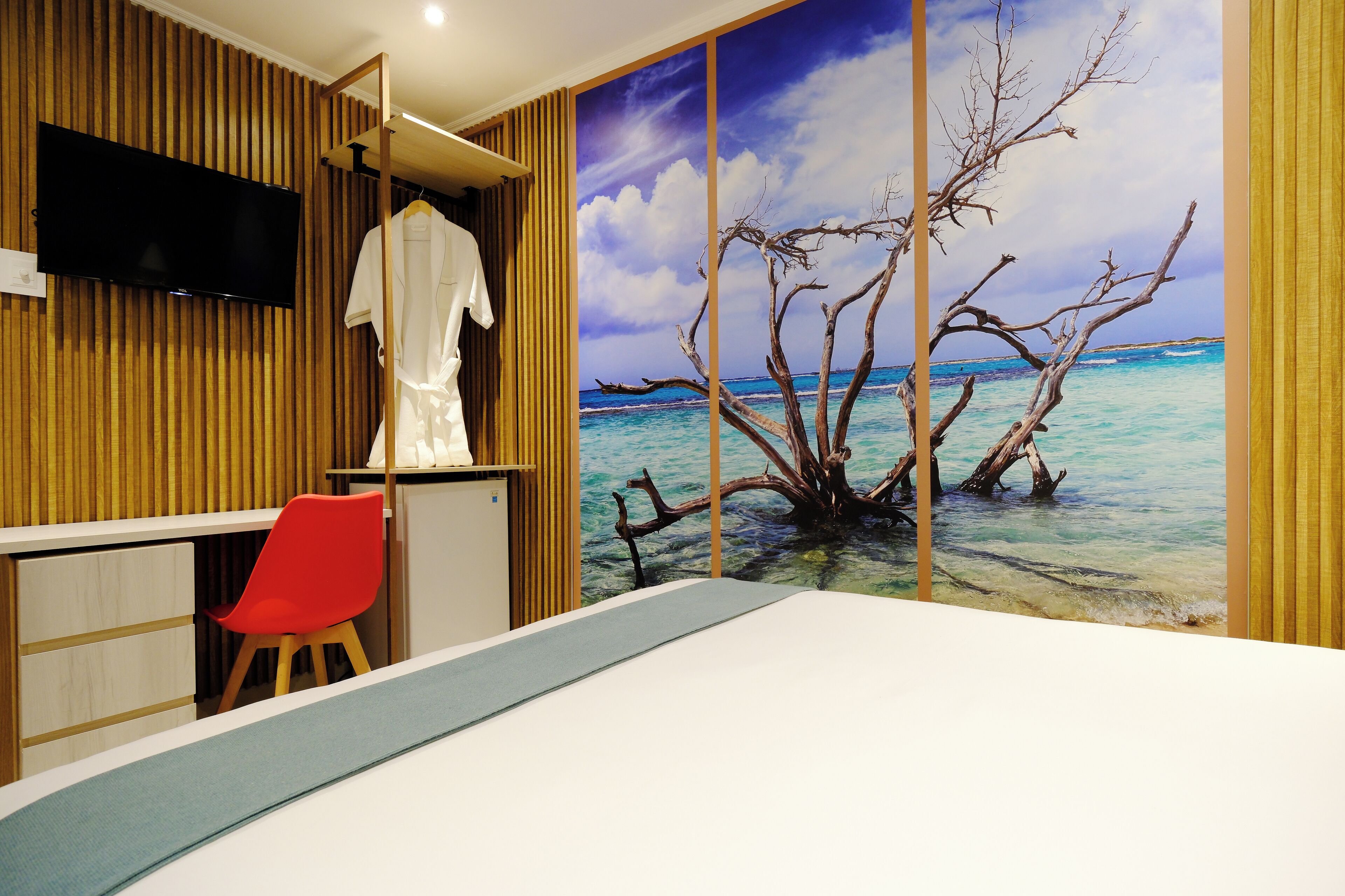 A bedroom with a large bed, a red chair, a TV mounted on a wooden wall, and a beach mural.