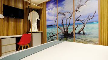A bedroom with a large bed, a red chair, a TV mounted on a wooden wall, and a beach mural.