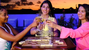 Trois personnes trinquent avec des verres de vin autour d’une table à carreaux, le tout se déroulant sur fond de coucher de soleil.