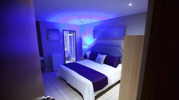 A bedroom with a bed, nightstands, a mirror, and a wall-mounted light fixture.