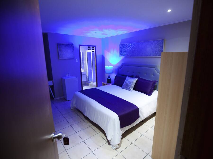 A bedroom with a bed, nightstands, a mirror, and a wall-mounted light fixture.