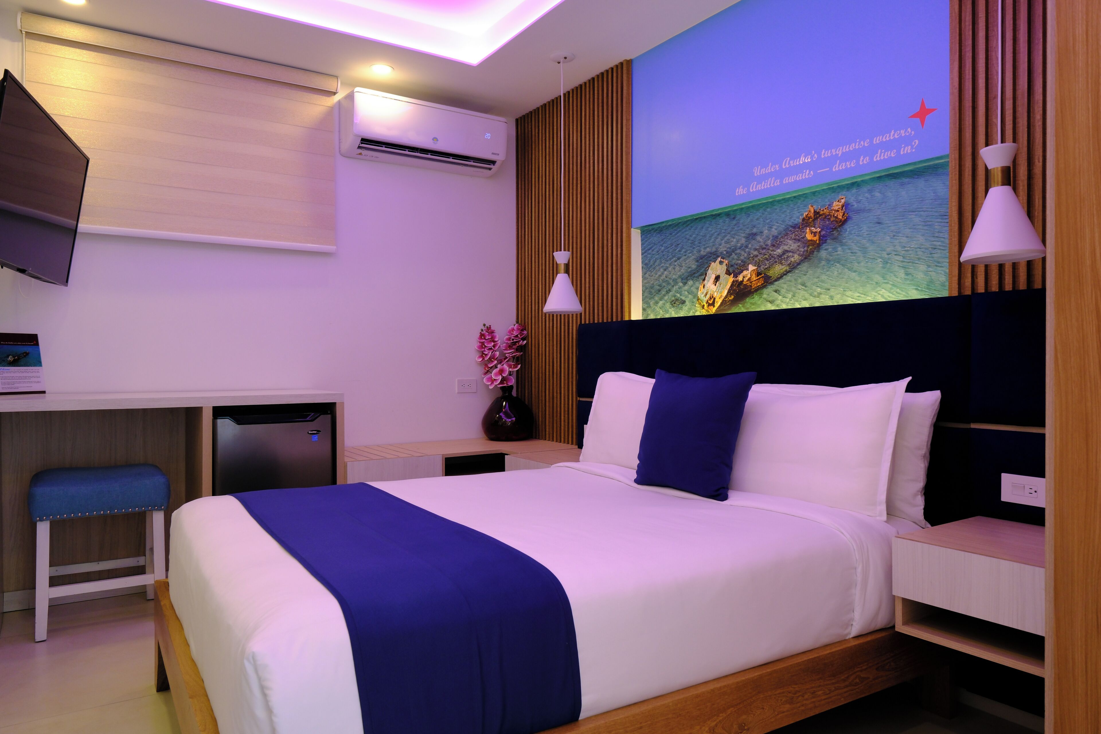 Ein modernes Hotelzimmer mit Bett, Nachttischen, einem Schreibtisch und einem an der Wand befestigten Fernseher.