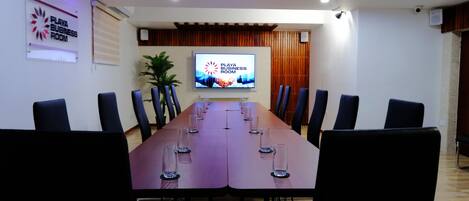 A conference room with a long table, chairs, a television screen, and a sign indicating it is the Playa Business Room.