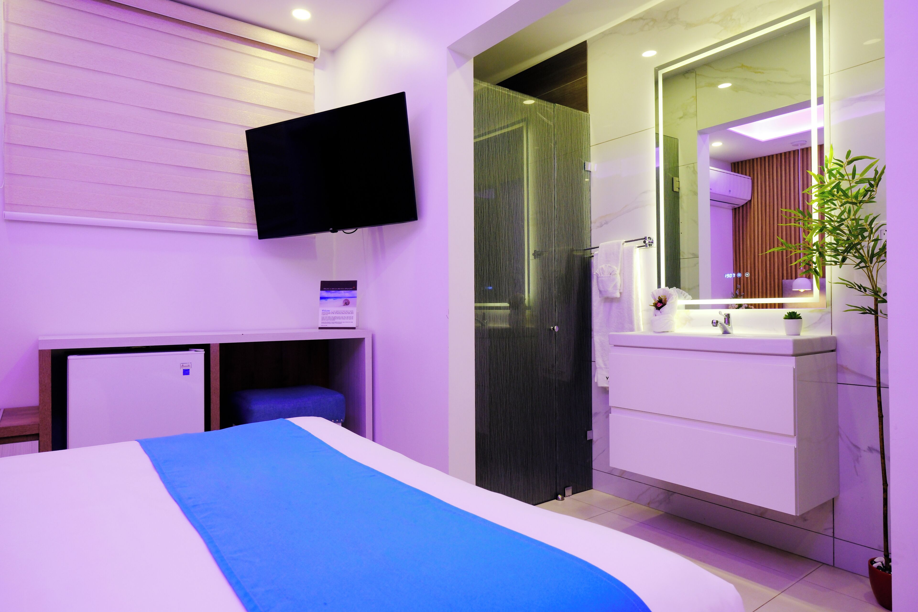 Una moderna camera d'hotel con un letto, una TV a parete, un angolo doccia e un bagno con un grande specchio.