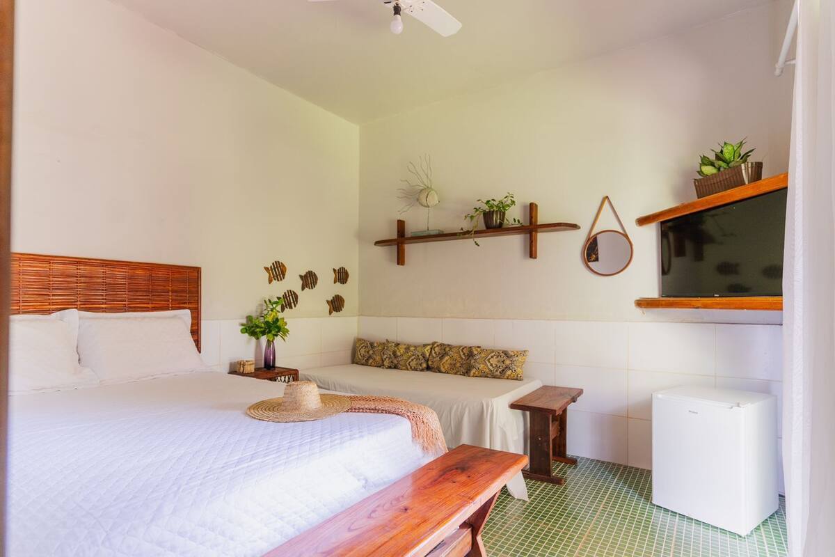 Une chambre à coucher avec un lit, une table de chevet et un petit bureau. On y trouve des décorations murales représentant des poissons, une plante et une étagère avec un miroir et un téléviseur.
