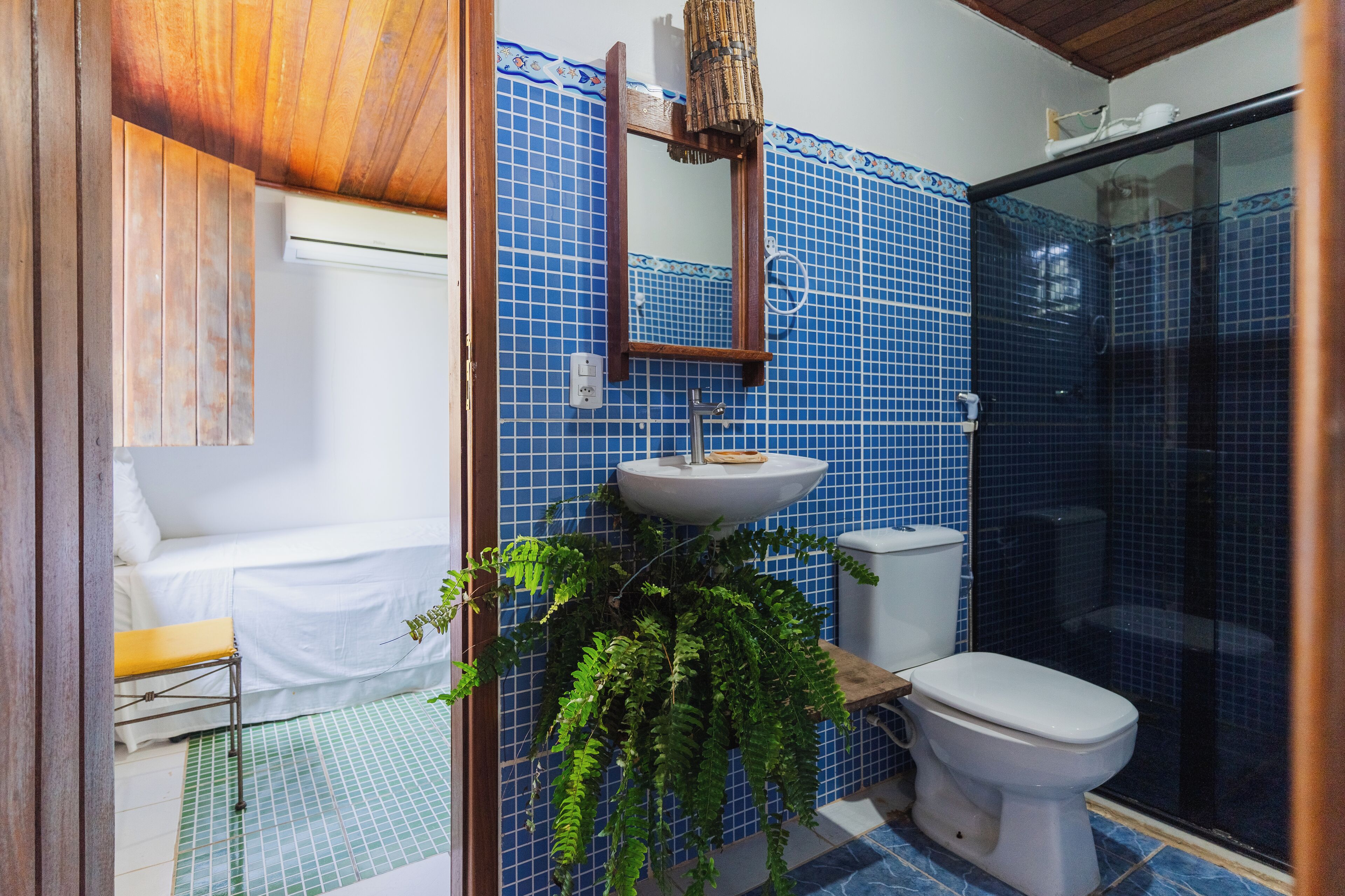 Un bany amb una paret revestida de rajoles blaves, un lavabo blanc, un vàter i una banca de fusta.