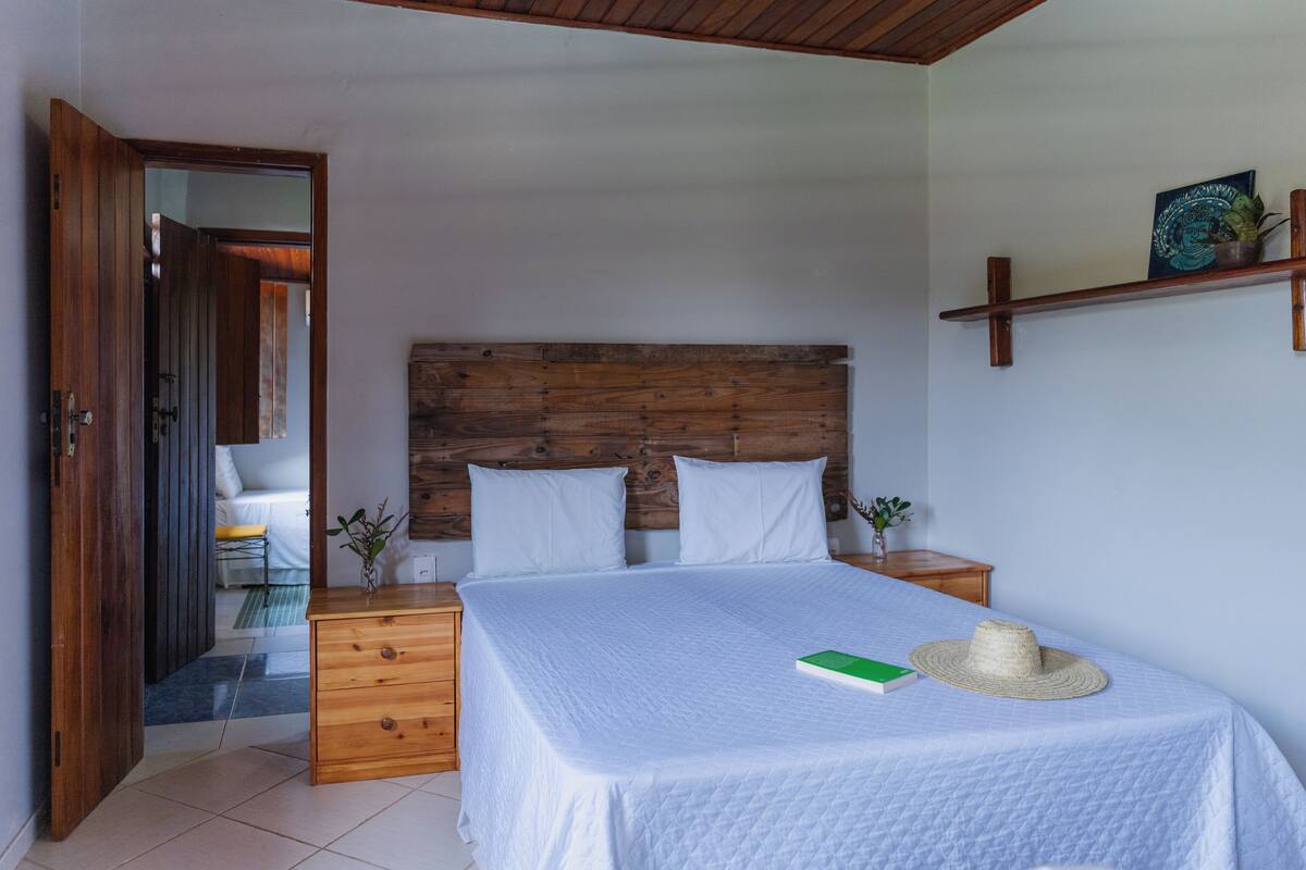 Une chambre à coucher avec une tête de lit en bois, un lit avec une literie blanche, une table de chevet avec une lampe et une commode en bois.