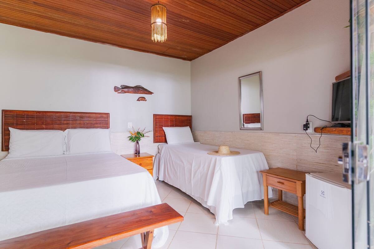 Une chambre d’hôtel avec deux lits, un banc en bois, une petite table, un miroir et un téléviseur.