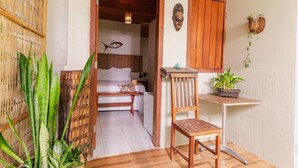 Una habitación con una cama, una silla de madera, una mesita pequeña y un estante en la pared con plantas.